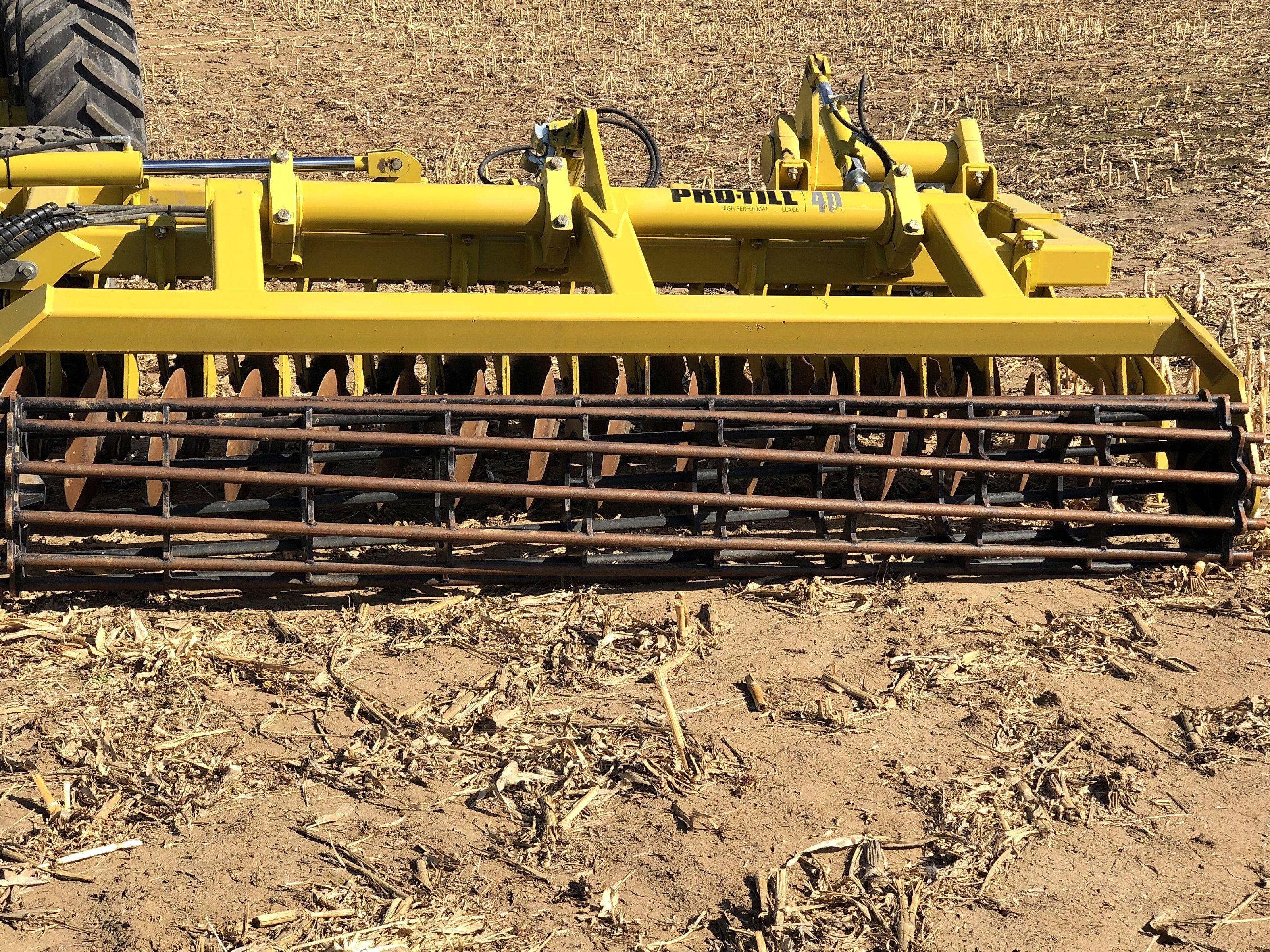 A tillage disc and its rolling basket close up in corn stubble, the tractor's tire at the edge of the frame