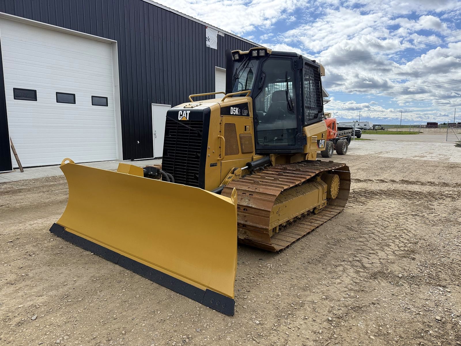 A small dozer standing beside the shop with its blade down