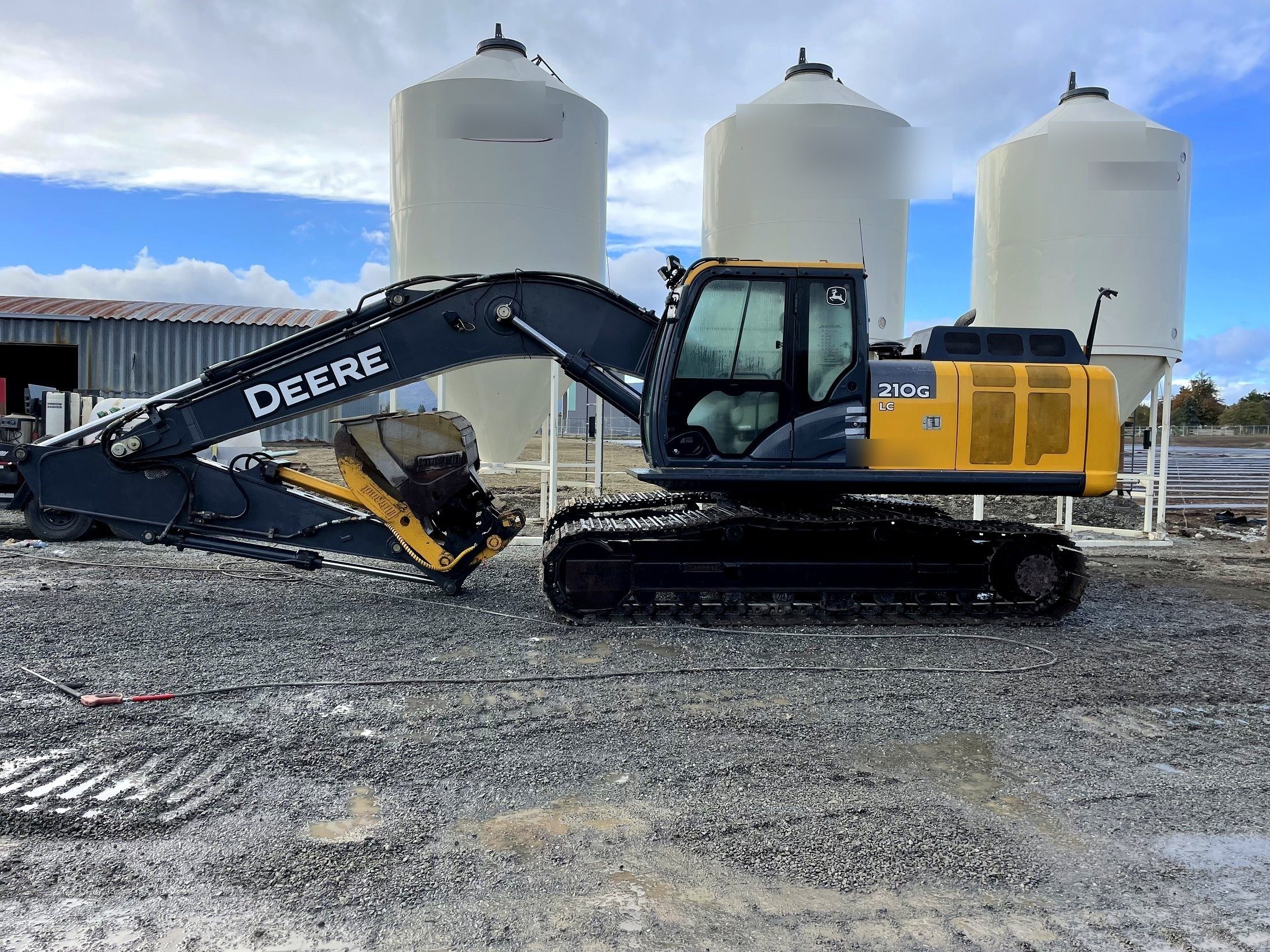 A tracked excavator in the yard beside the feed bins, side on