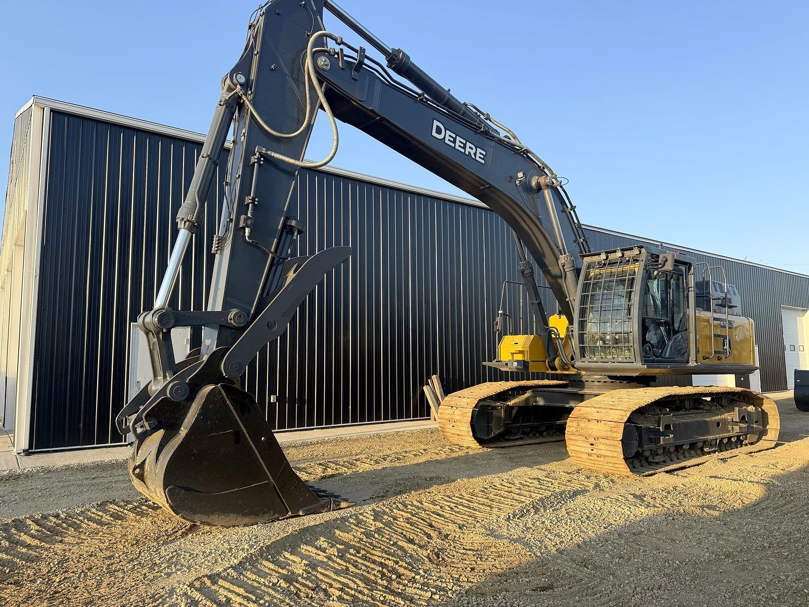 A large tracked excavator beside the shop, bucket down, side on