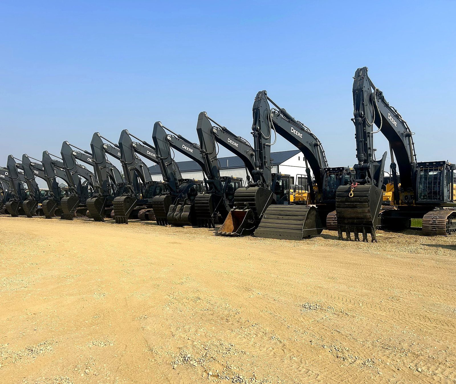 A row of excavators in the yard, booms up, on gravel