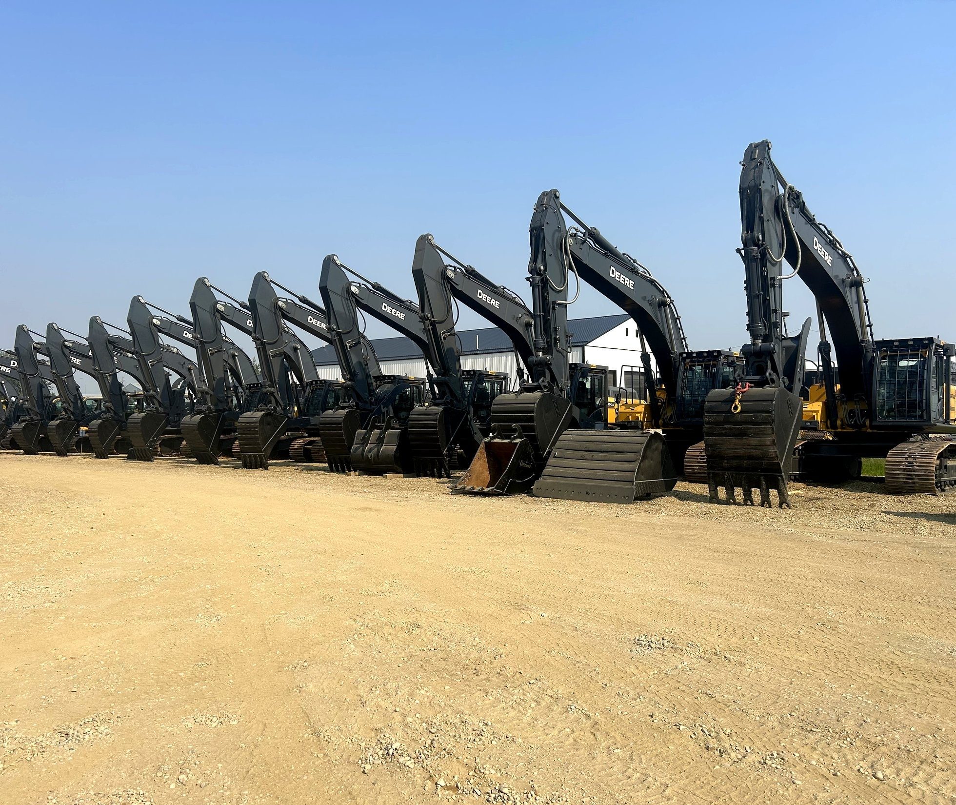 A row of excavators in the yard, booms up, side on, in sun