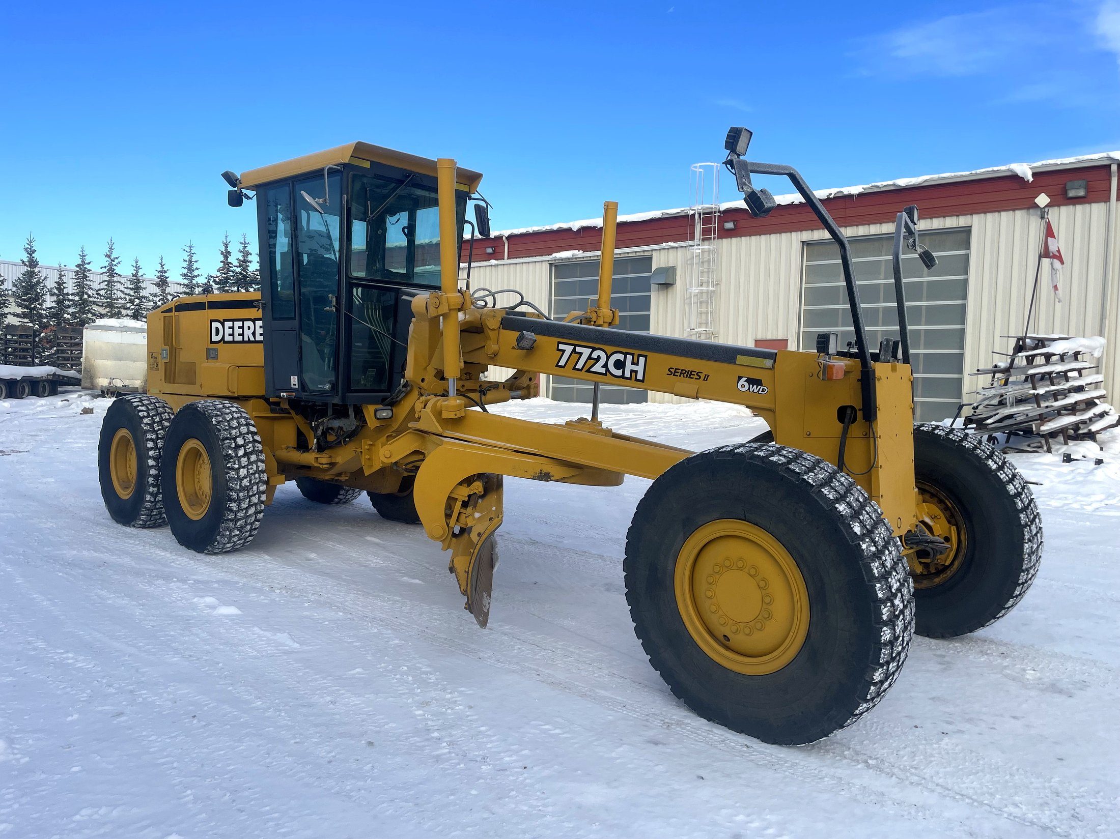 A motor grader in the yard in winter, blade angled