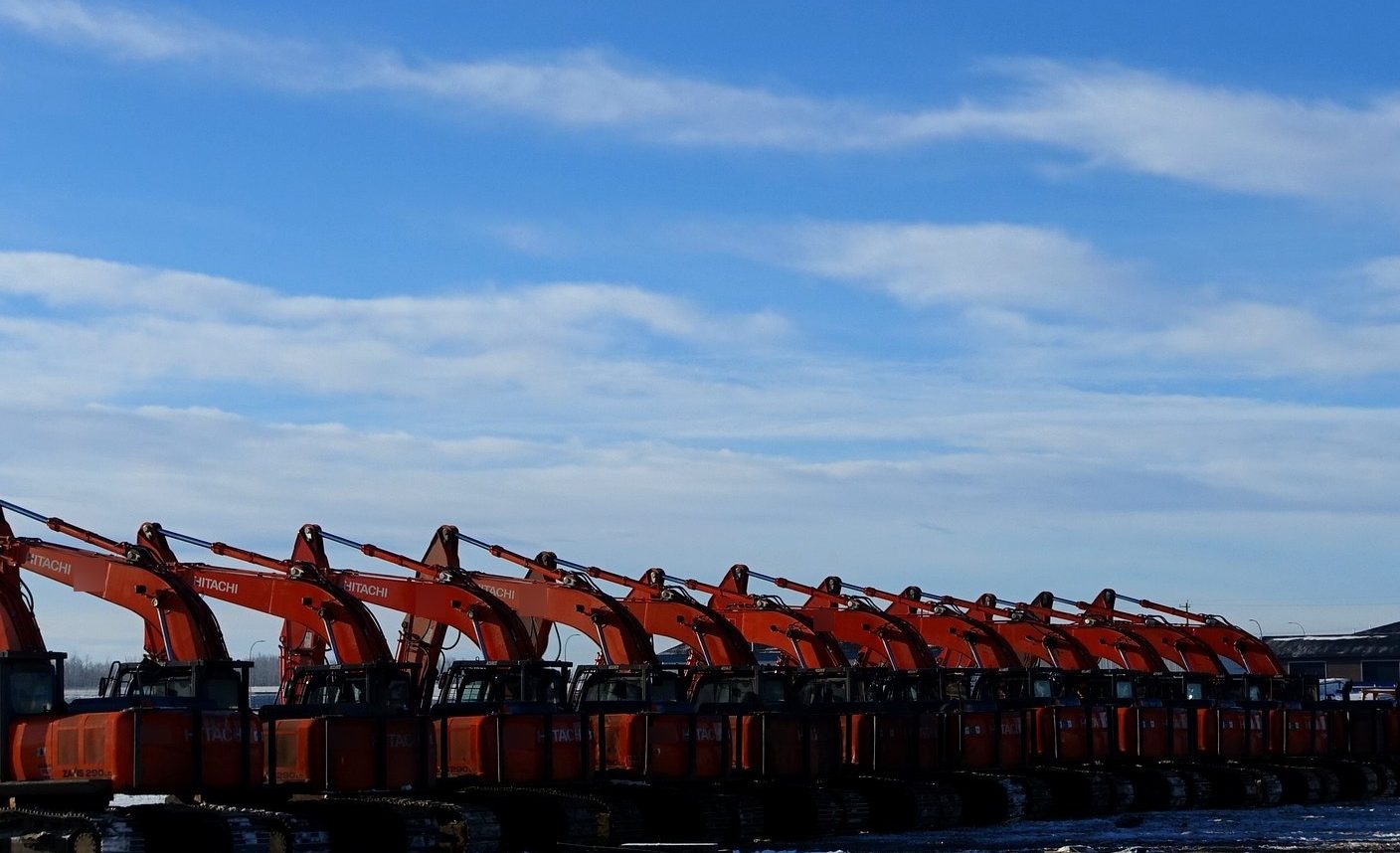 A row of excavators in the yard in winter, booms up, under a blue sky