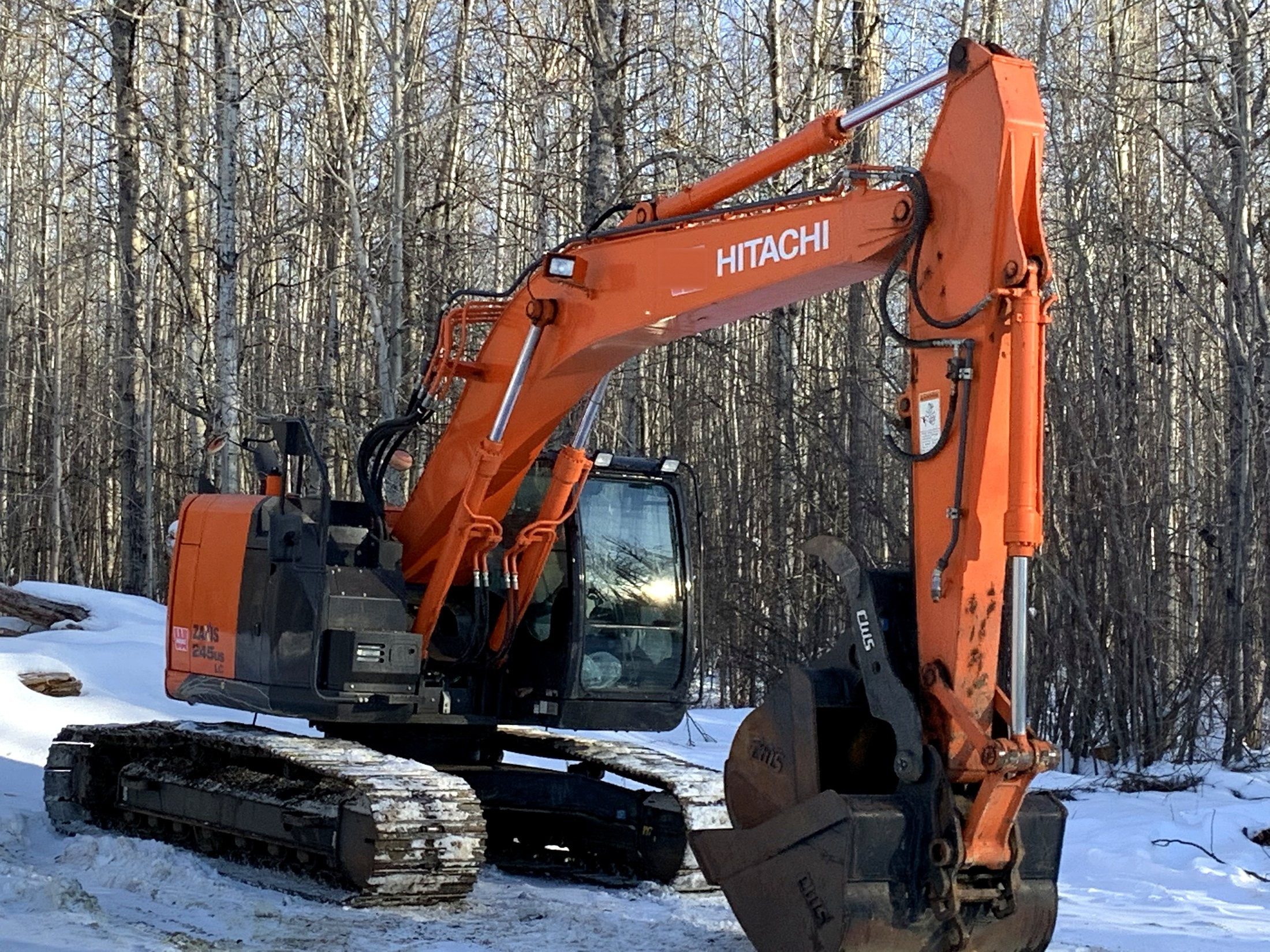 An excavator at a treeline in winter, snow on the ground