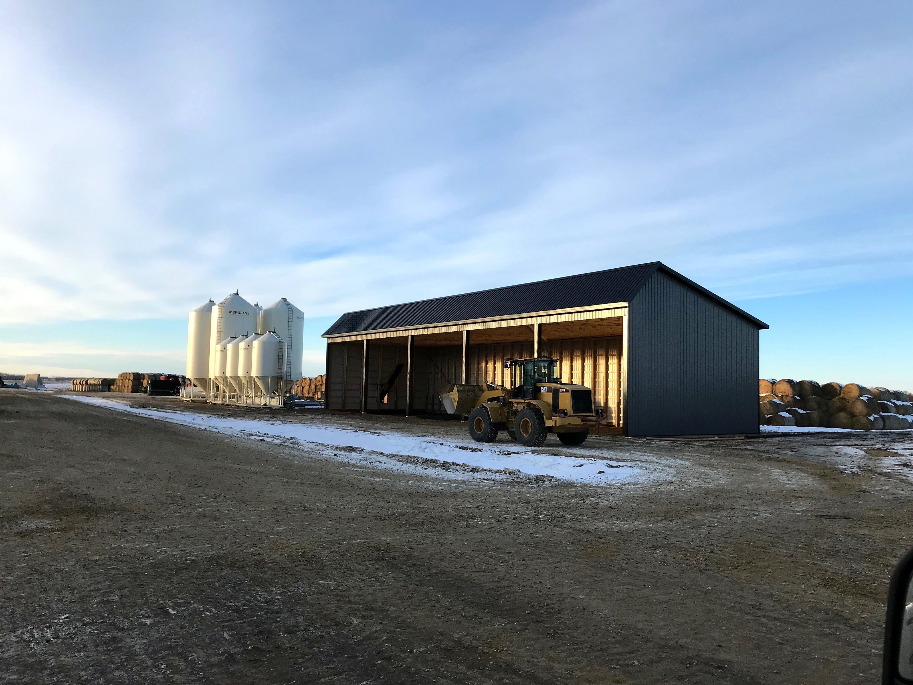 A wheel loader parked at the open end of a new feed shed in winter
