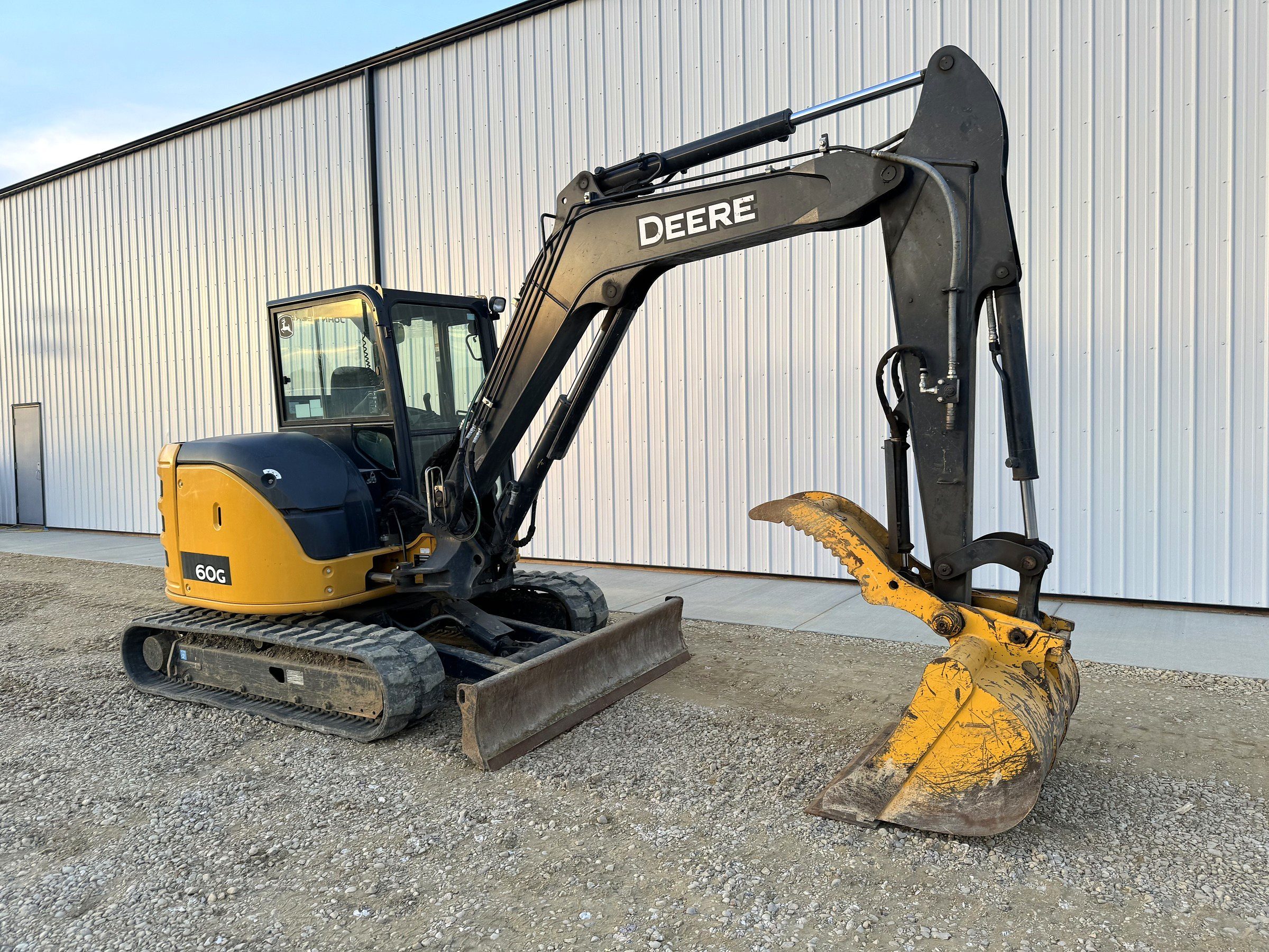 A mini excavator standing beside the shop with its bucket down