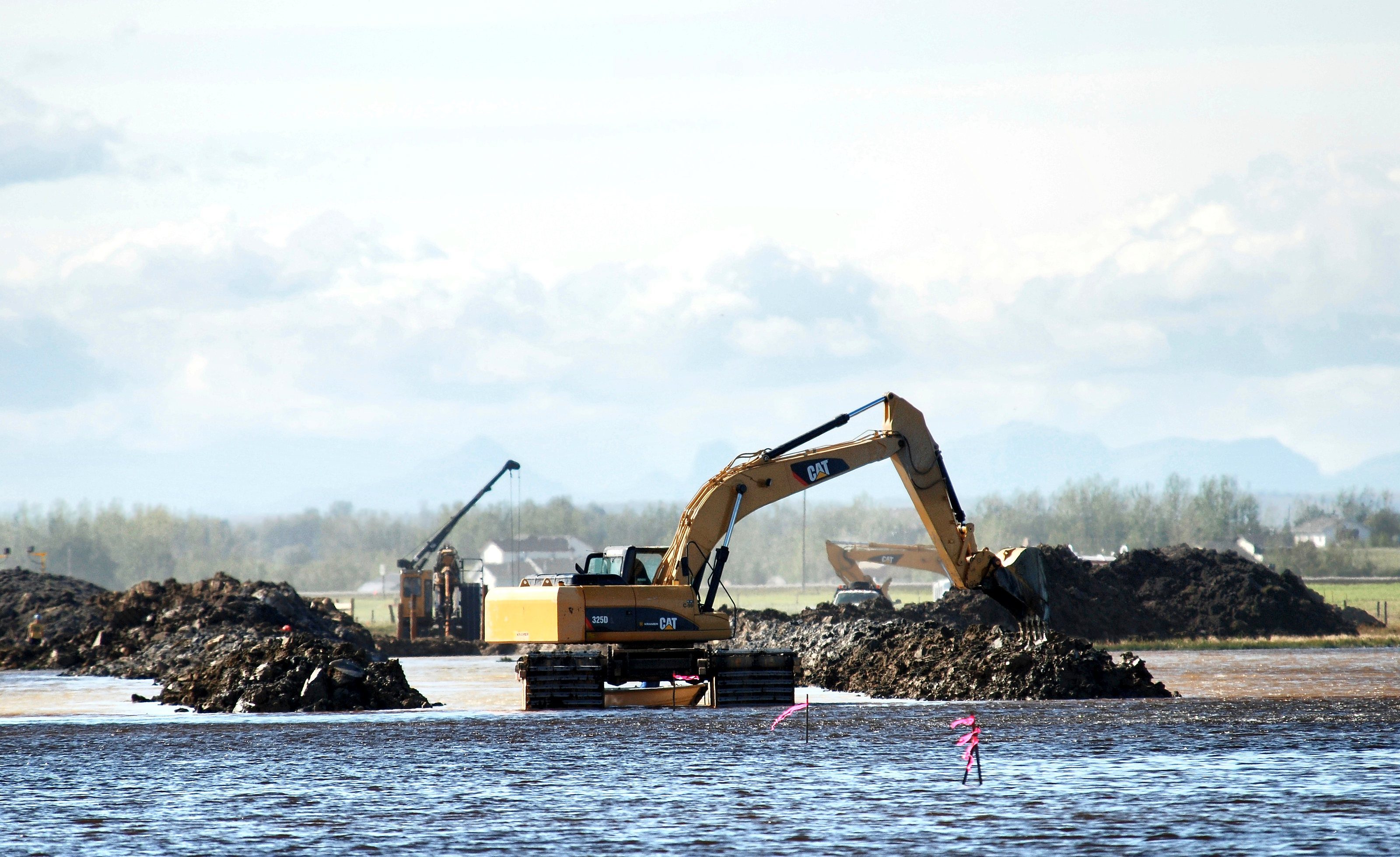 An excavator working from a berm at the water's edge, the boom out over open water