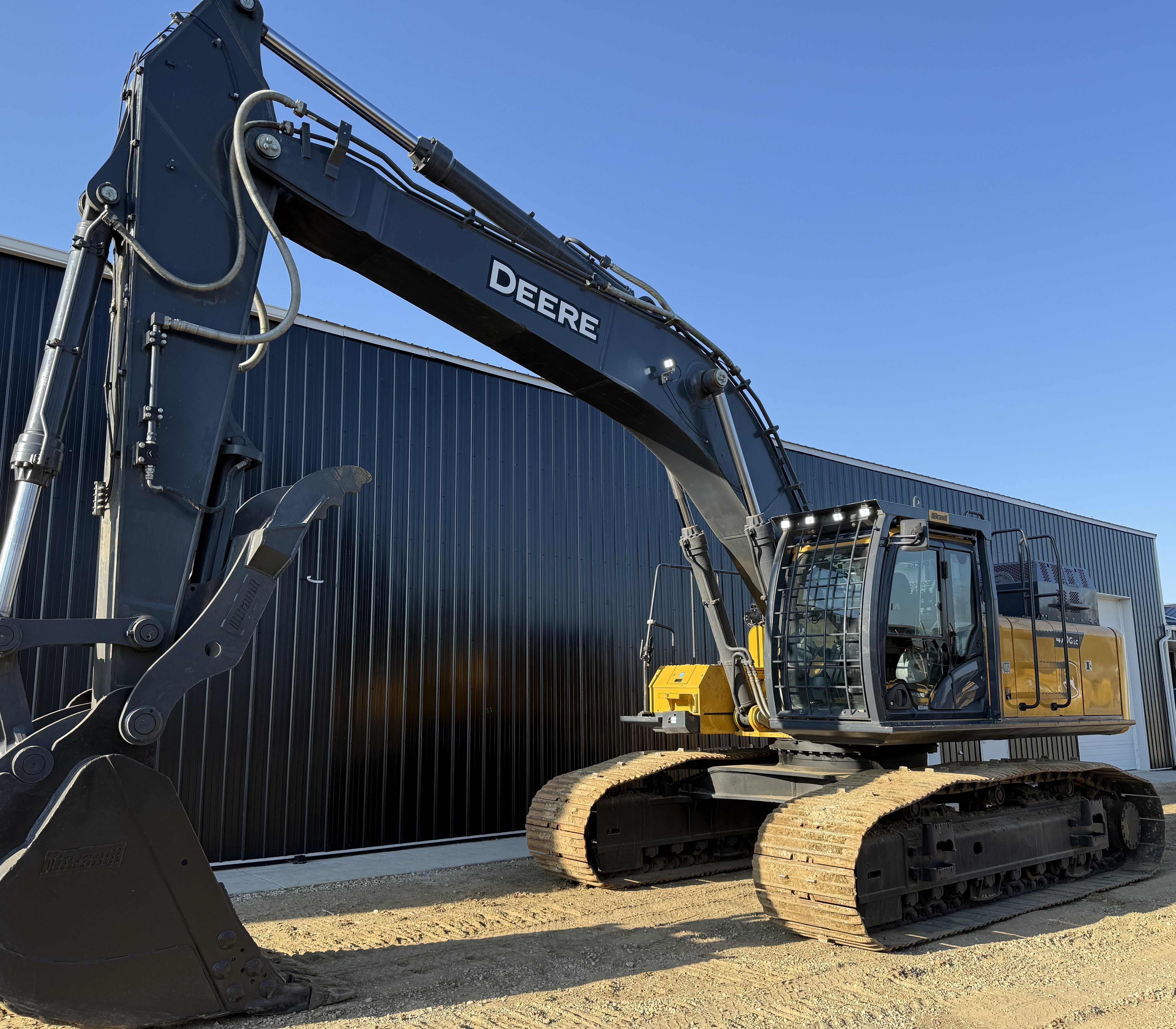 An excavator from low in front, boom and bucket raised against the sky