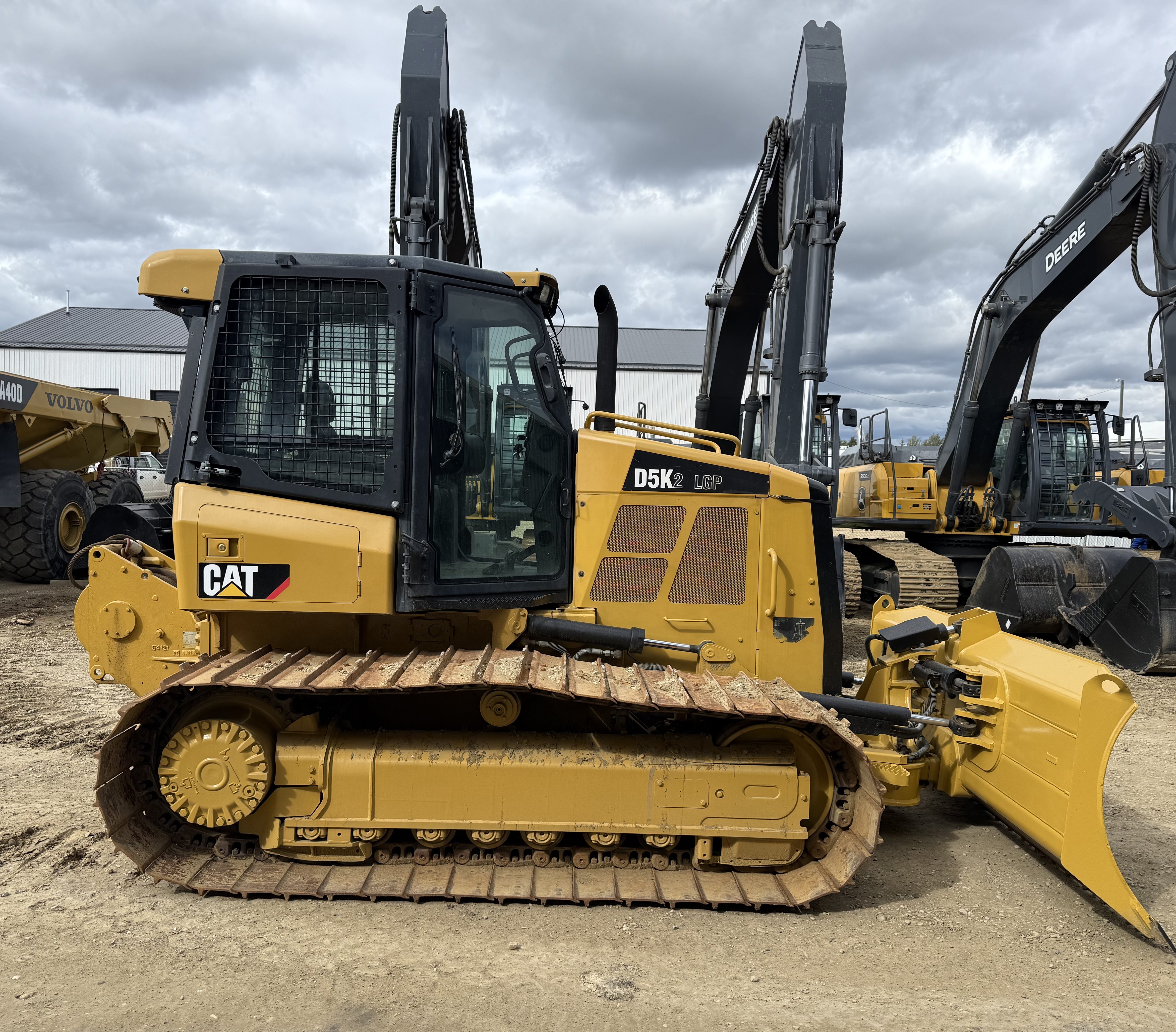 A dozer in the yard with a row of excavators behind it, booms up