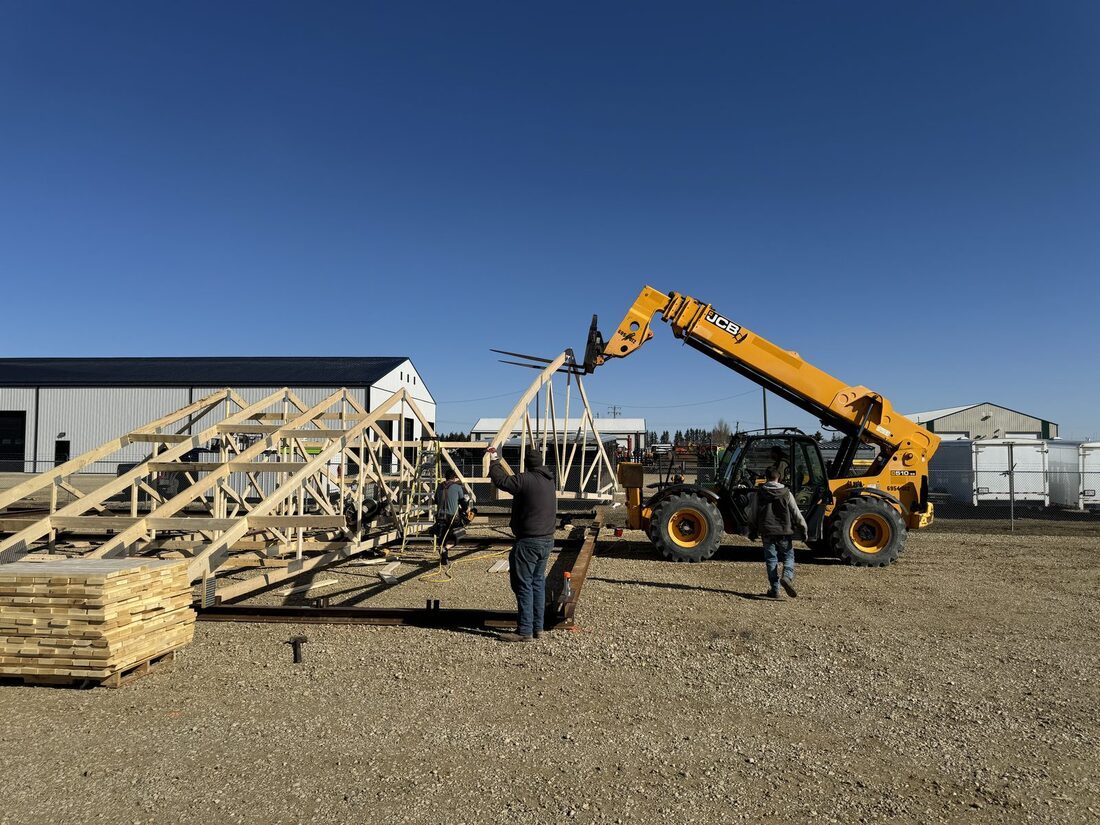 A telehandler lifting a roof truss with two people guiding it