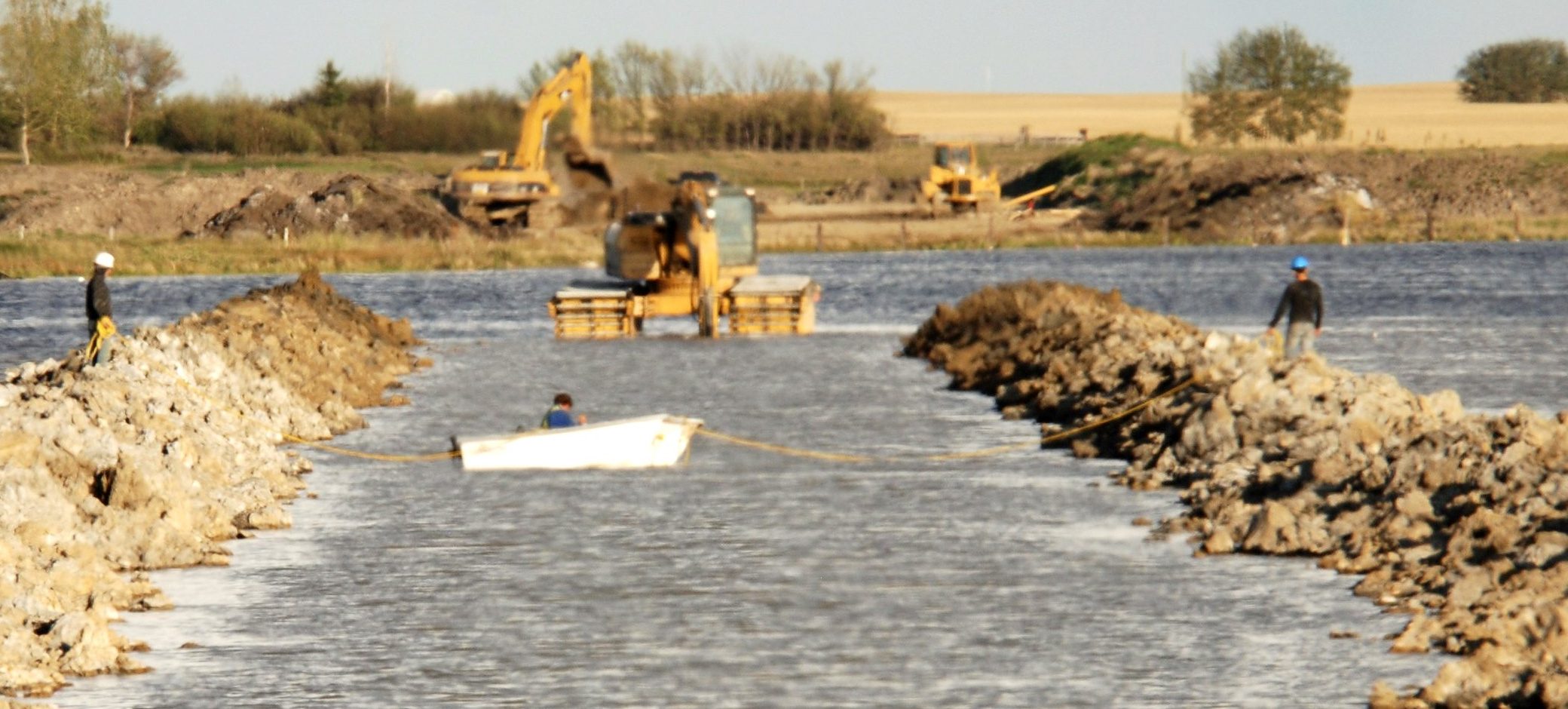 An excavator at the head of a rock channel cut through open water